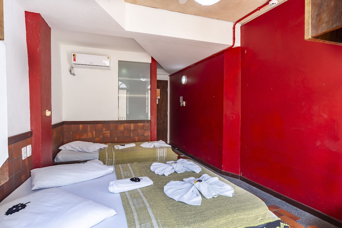 Ein Hotelzimmer mit zwei Betten, roten Wänden, einem hölzernen Kopfteil, einer weißen Klimaanlage und Handtüchern auf dem Boden.