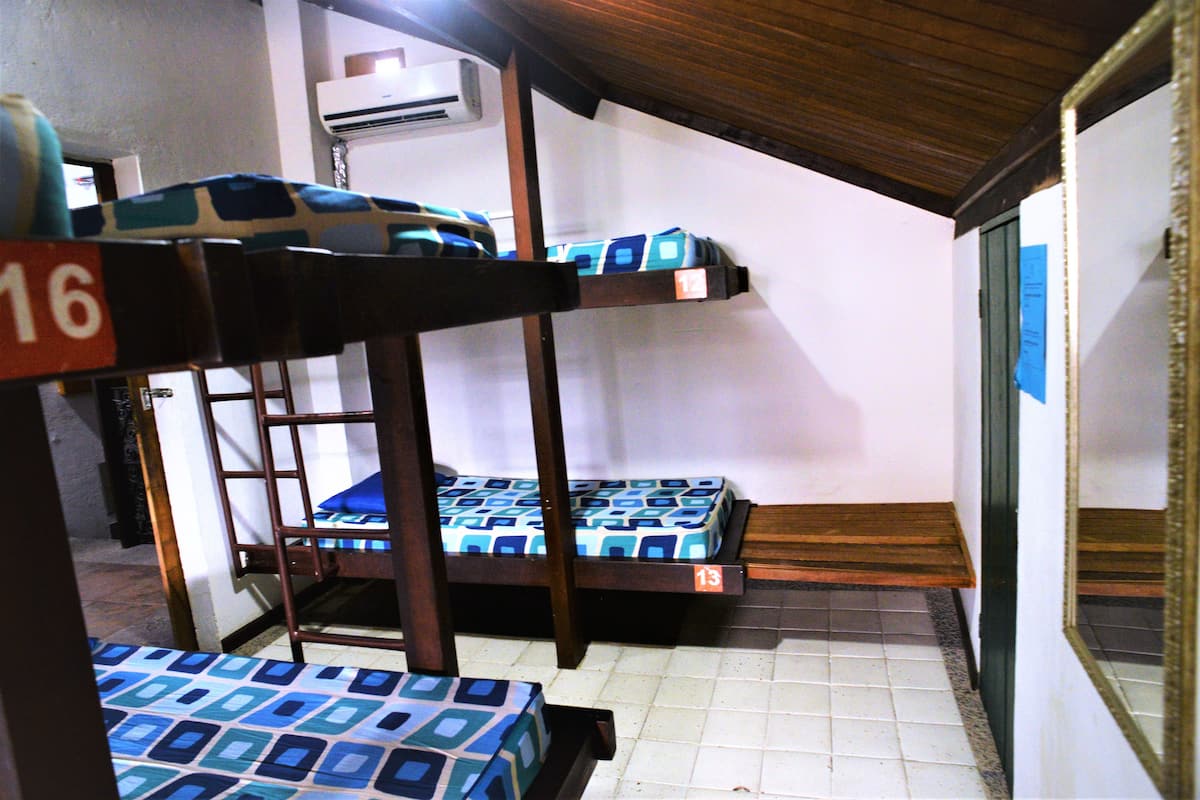 Ein Schlafsaalzimmer mit Stockbetten, Fliesenboden und Holzbalkendecke.