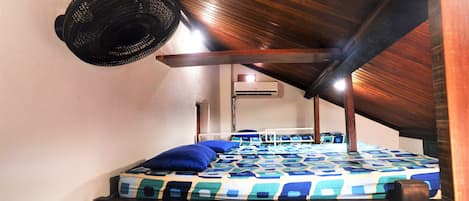 Una cama litera con una colcha estampada, un ventilador colgante y una unidad de aire acondicionado al fondo.