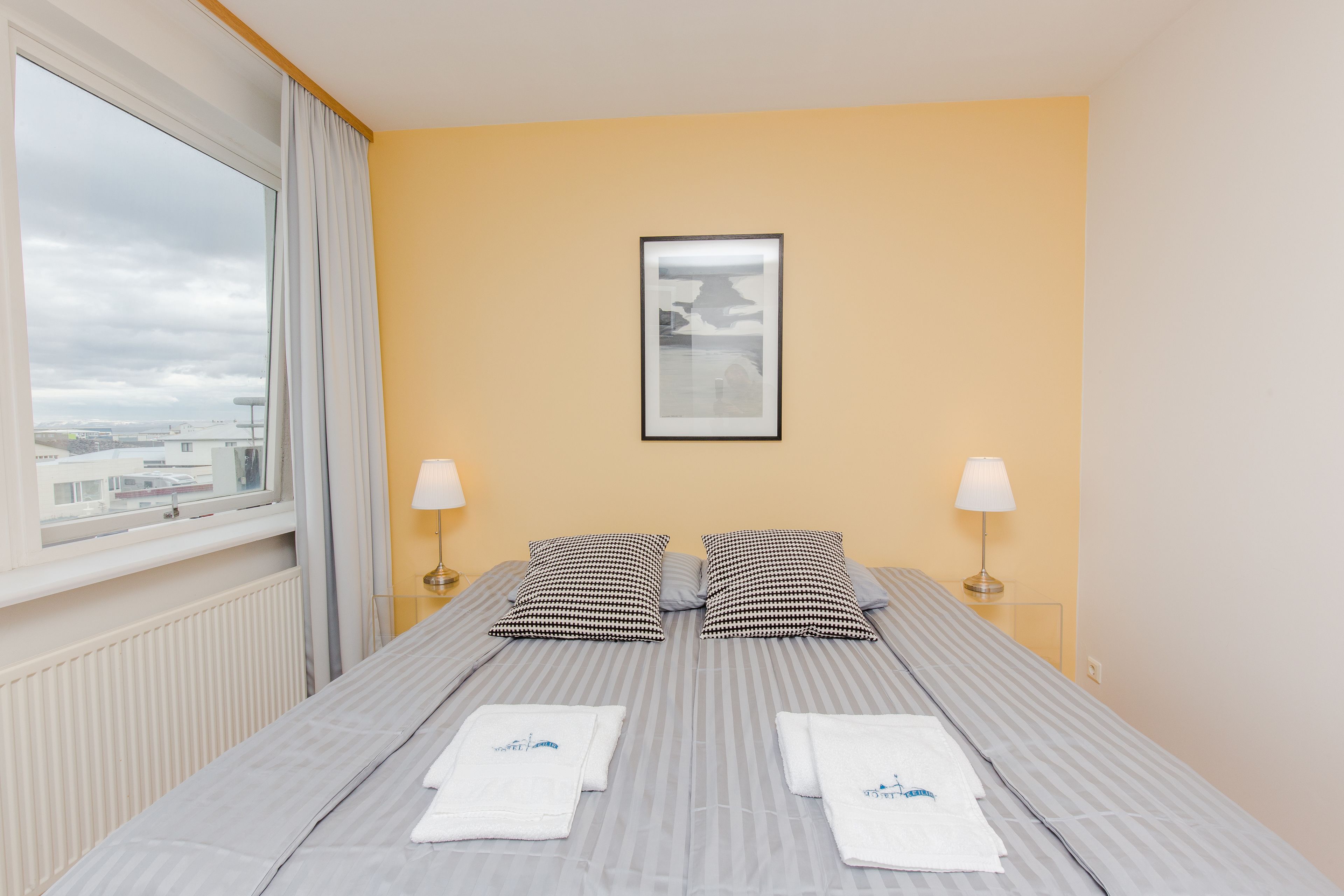 A hotel room with a bed, two pillows, a framed picture on the wall, and a window with curtains.