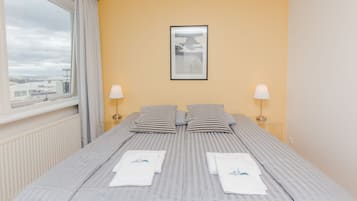 A hotel room with a bed, two pillows, a framed picture on the wall, and a window with curtains.