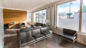 A modern waiting area with leather seating, a small table with a lamp, and large windows offering a view of the city.