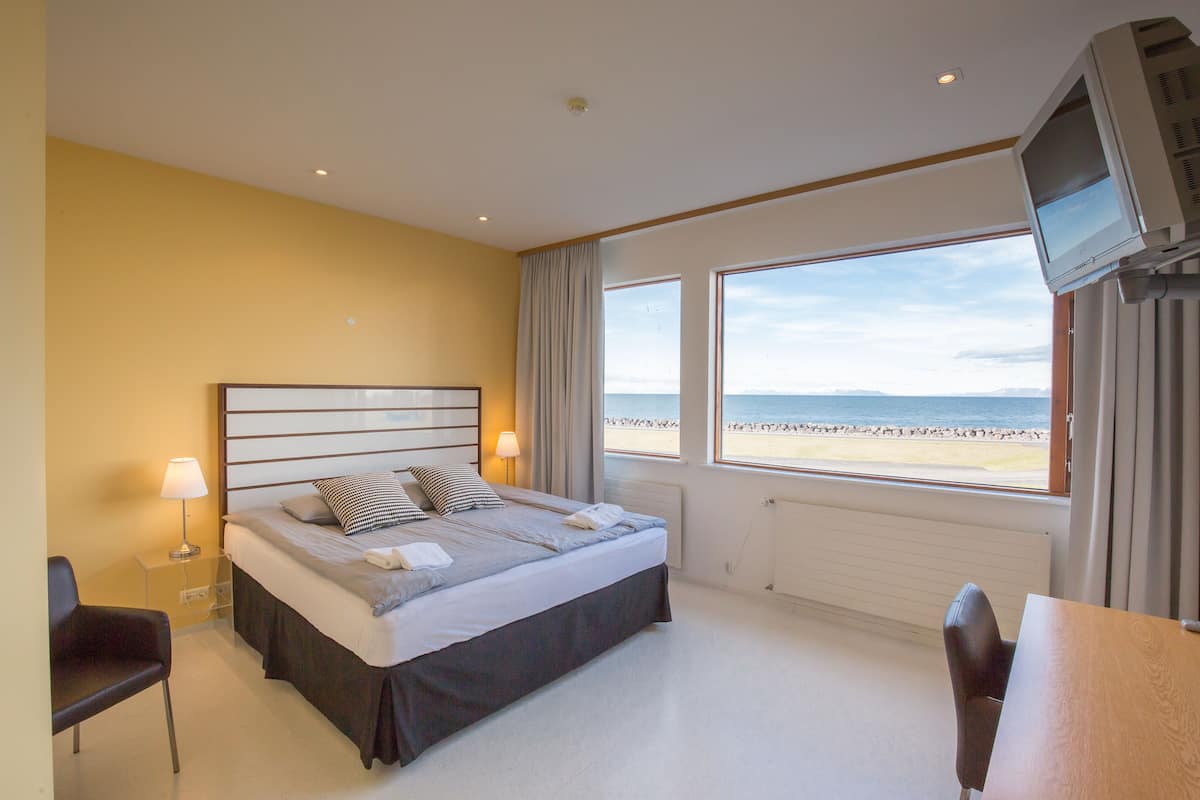 A hotel room with a bed, bedside tables, a TV, and a view of the beach.