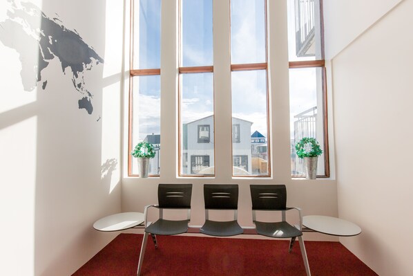 A waiting area with three chairs, a red carpet, and a large window with a view of buildings and a map on the wall.