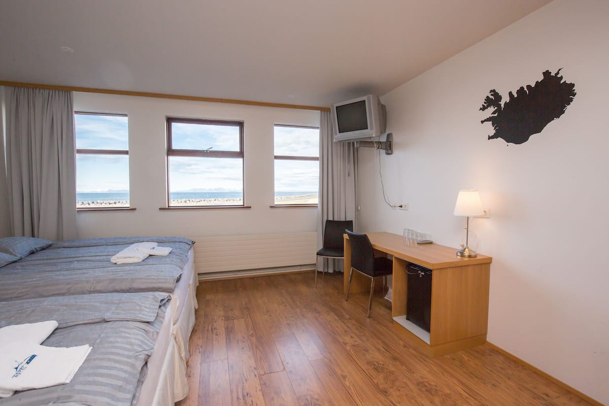 A hotel room with two beds, a desk, a chair, a TV, and a view of the beach.