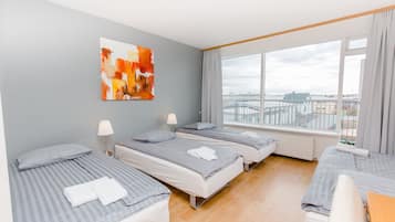 A hotel room with three beds, a large window with a view, and a painting on the wall.