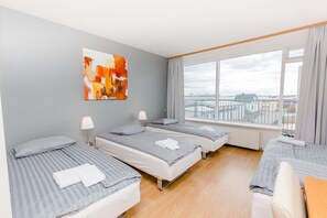 A hotel room with three beds, a large window with a view, and a painting on the wall.