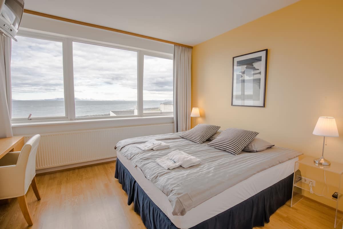 A hotel room with a large bed, a desk, and a view of the sea.