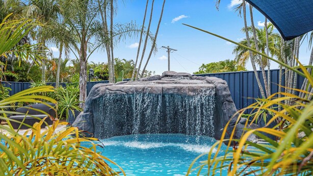 Une piscine agrémentée d’une cascade et entourée d’une végétation tropicale.