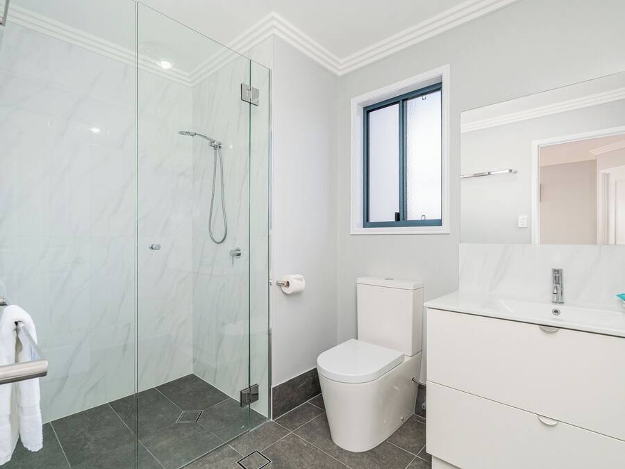 A modern bathroom with a glass shower enclosure, a toilet, and a vanity with a mirror.