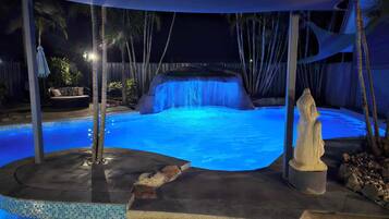 Relax by the illuminated pool surrounded by palm trees and a waterfall feature.