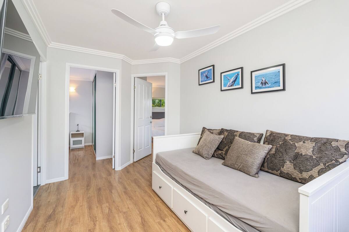 A bedroom with a bed, a ceiling fan, and framed pictures on the wall.