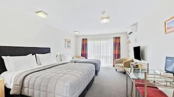 A hotel room with a large bed, a desk with a chair, a TV, and a window with curtains.