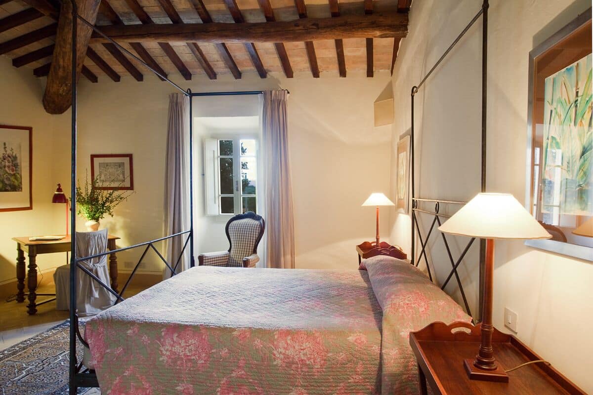 Ein Schlafzimmer mit einem Bett, zwei Nachttischlampen, einem Sessel, einem Tisch und einem Fenster mit Vorhängen.