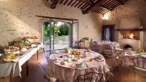 A rustic dining area with round tables covered in tablecloths, a fireplace, and a view of the outdoors. - Borgo della Marmotta - Farm Home (Spoleto)