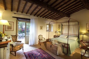 Un dormitorio tradicional con cama con dosel, un sillón, una mesita de noche y un amplio ventanal con cortinas.