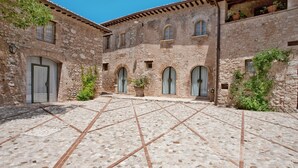 A courtyard with stone flooring and arched doorways, surrounded by stone buildings with potted plants. - Borgo della Marmotta - Farm Home (Spoleto)