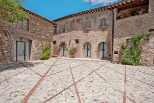 Un patio con suelo de piedra y arcos, rodeado de edificios de piedra y macetas con plantas.