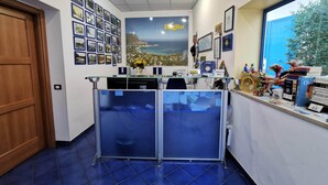 A reception area with a counter, framed photos on the wall, a large window with a view, and a door. - Al Baglio - Affittacamere (Palermo)