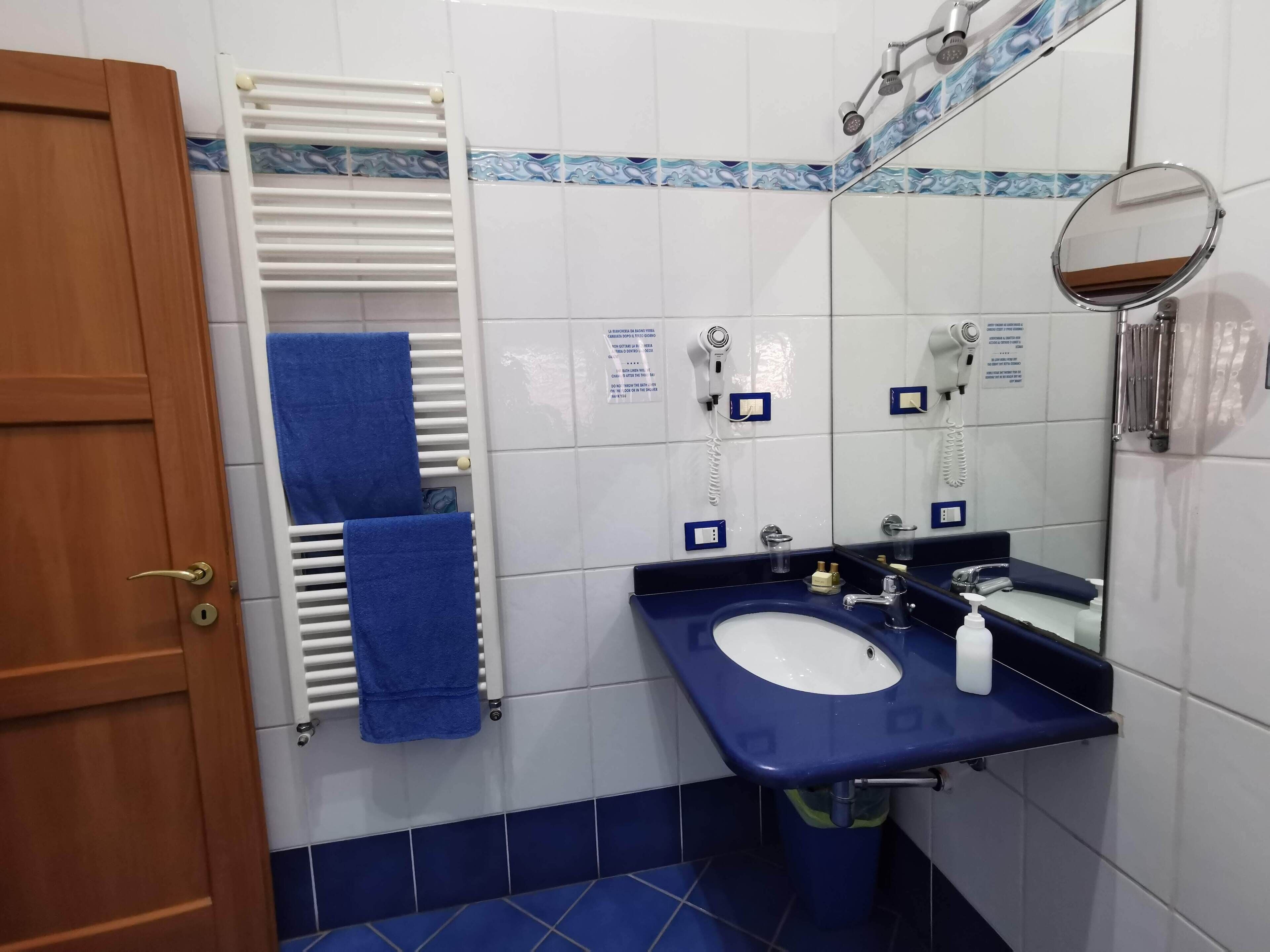 A bathroom with a white sink, blue tiles, a towel rack, a mirror, and a hairdryer.