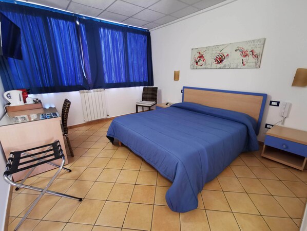 A hotel room with a bed, a desk, a chair, a radiator, and a painting on the wall. - Al Baglio - Affittacamere (Palermo)