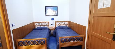 A small room with two wooden beds, a nightstand, a framed picture on the wall, and a door with a lock.