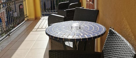 Un balcon avec une table ronde et des chaises en osier, donnant sur un quartier résidentiel.