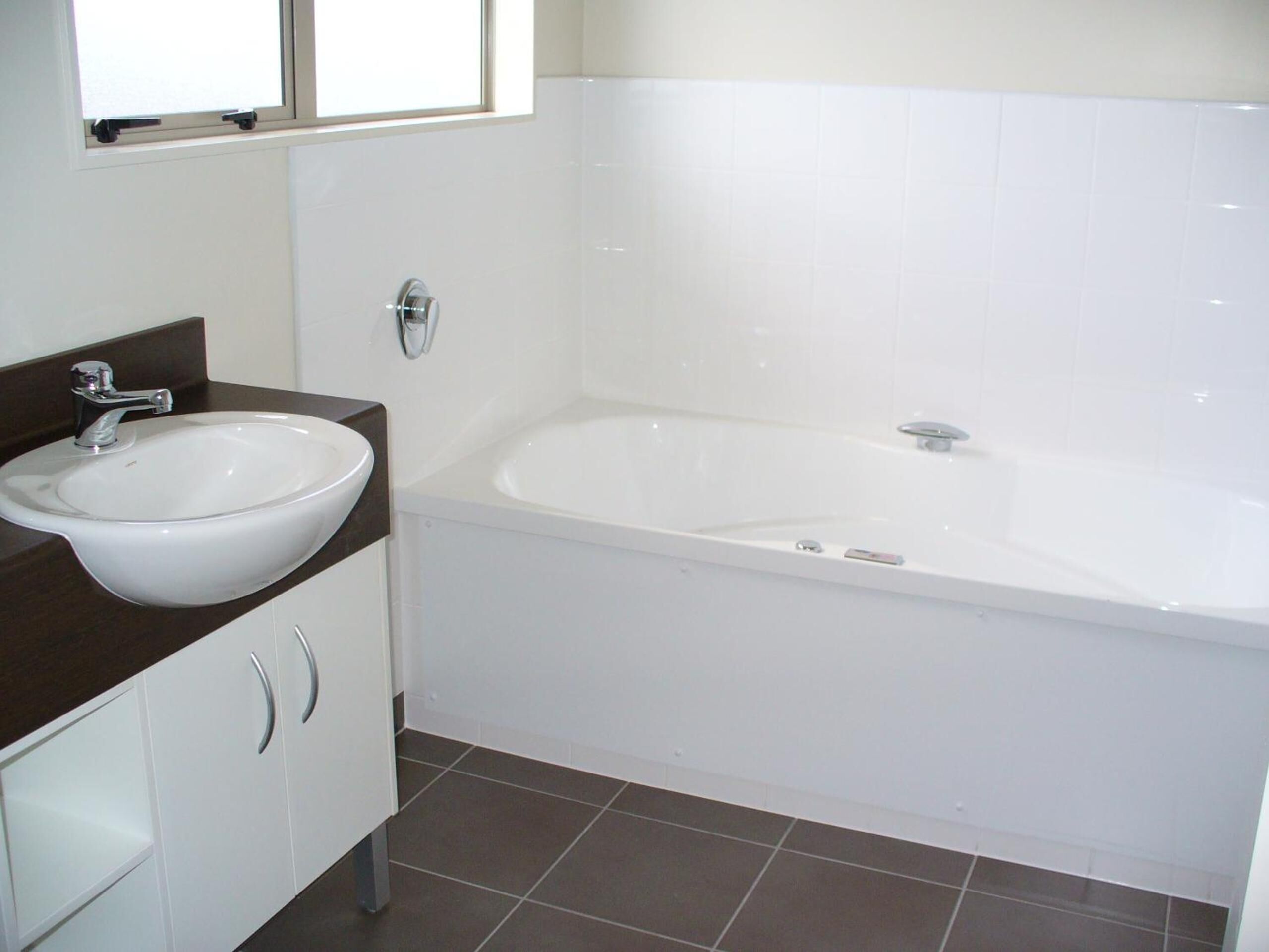 Un baño con un lavamanos blanco, una bañera y una ventana sobre el lavamanos.
