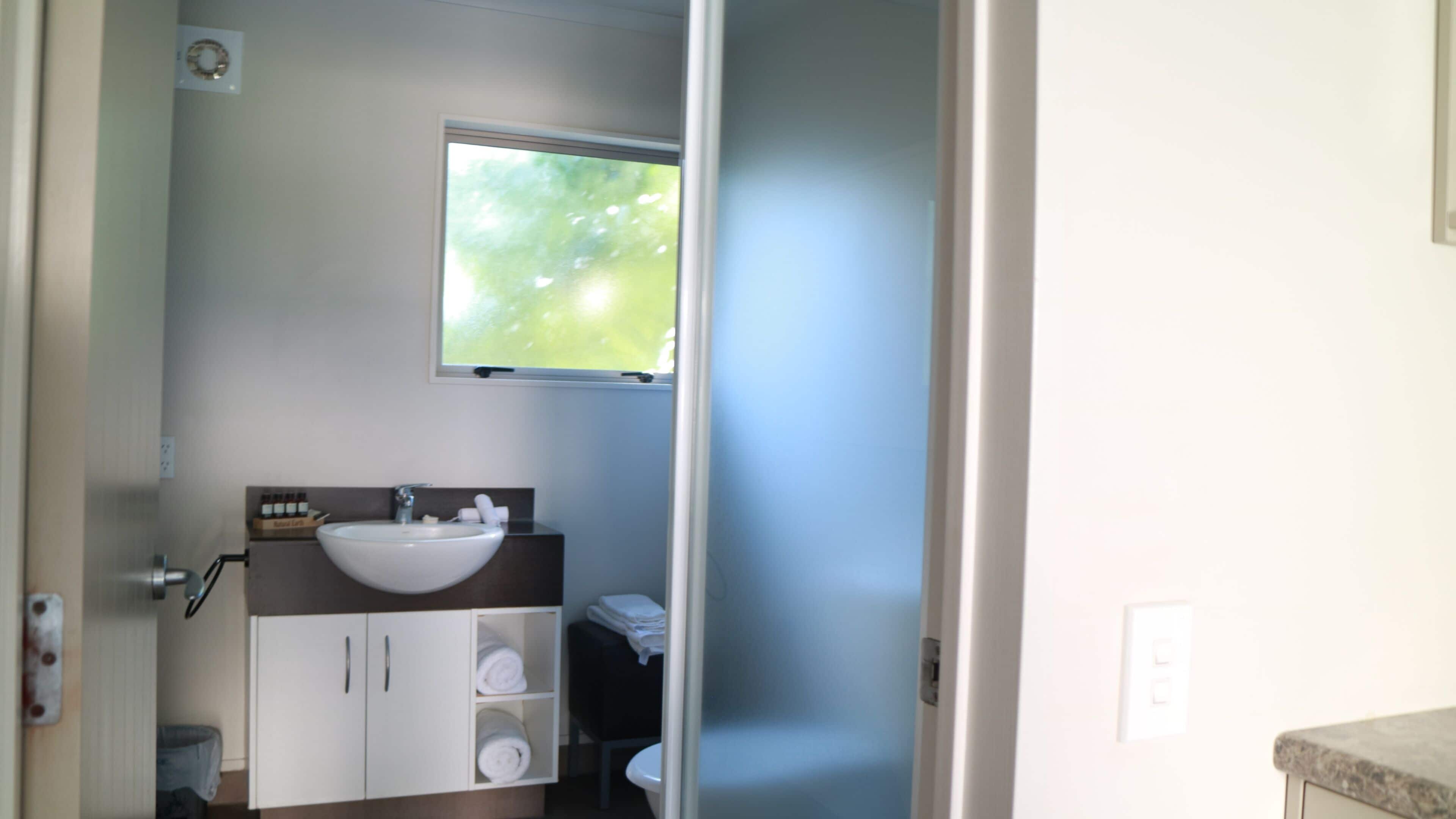 Une salle de bain avec un lavabo blanc, une fenêtre au-dessus et un porte-serviettes.