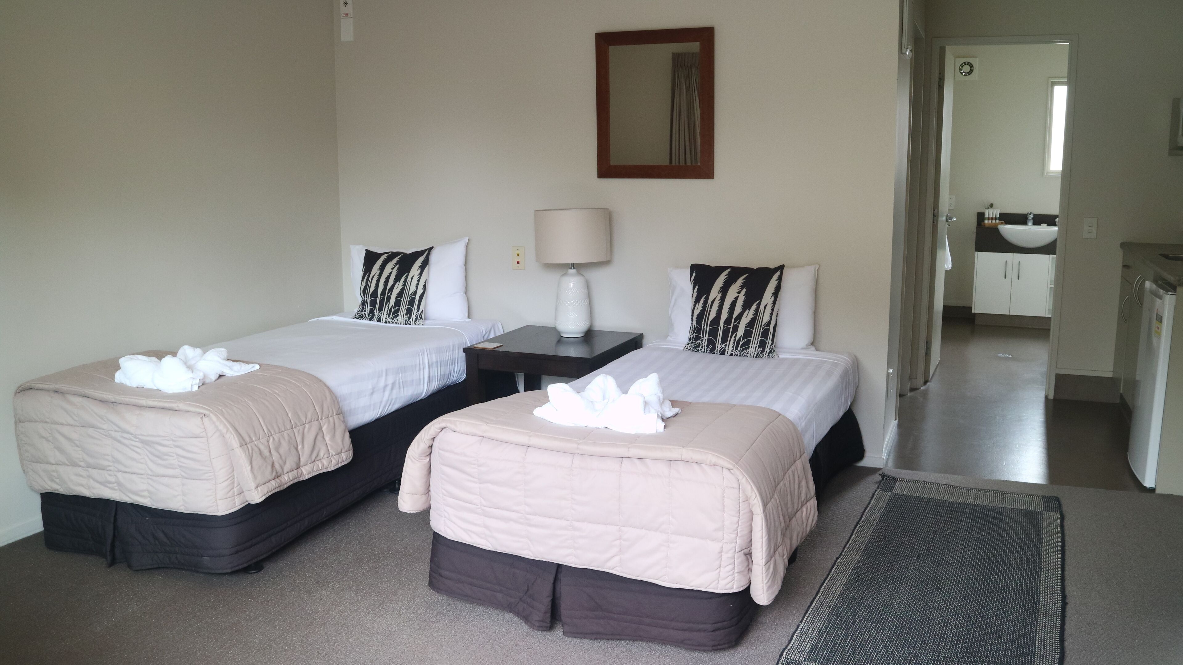 A hotel room with two beds, a nightstand, a lamp, and a bathroom visible through an open door.