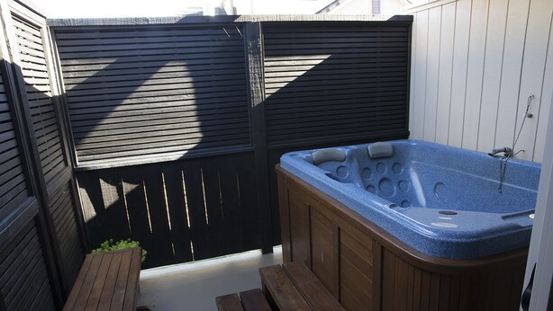 Een hottub met houten banken en een zwarte omheining in een achtertuin.