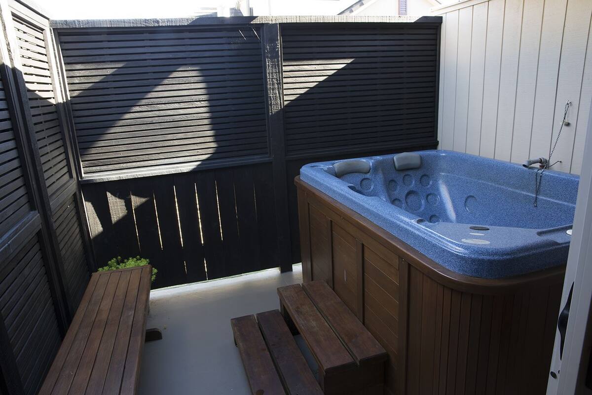 A hot tub with wooden benches and a black fence in a backyard.