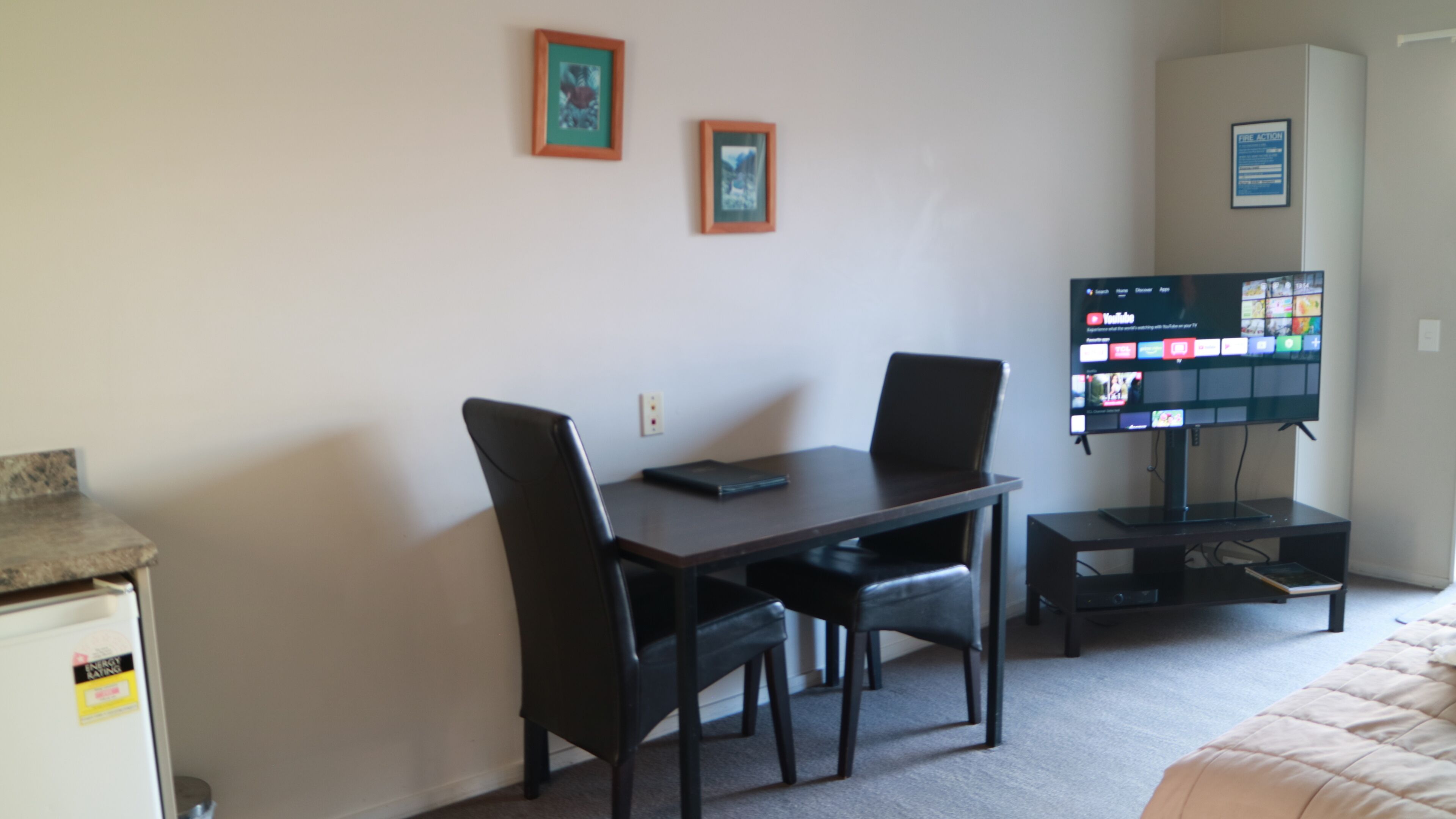 A hotel room with a desk, two chairs, a television, and a bed.