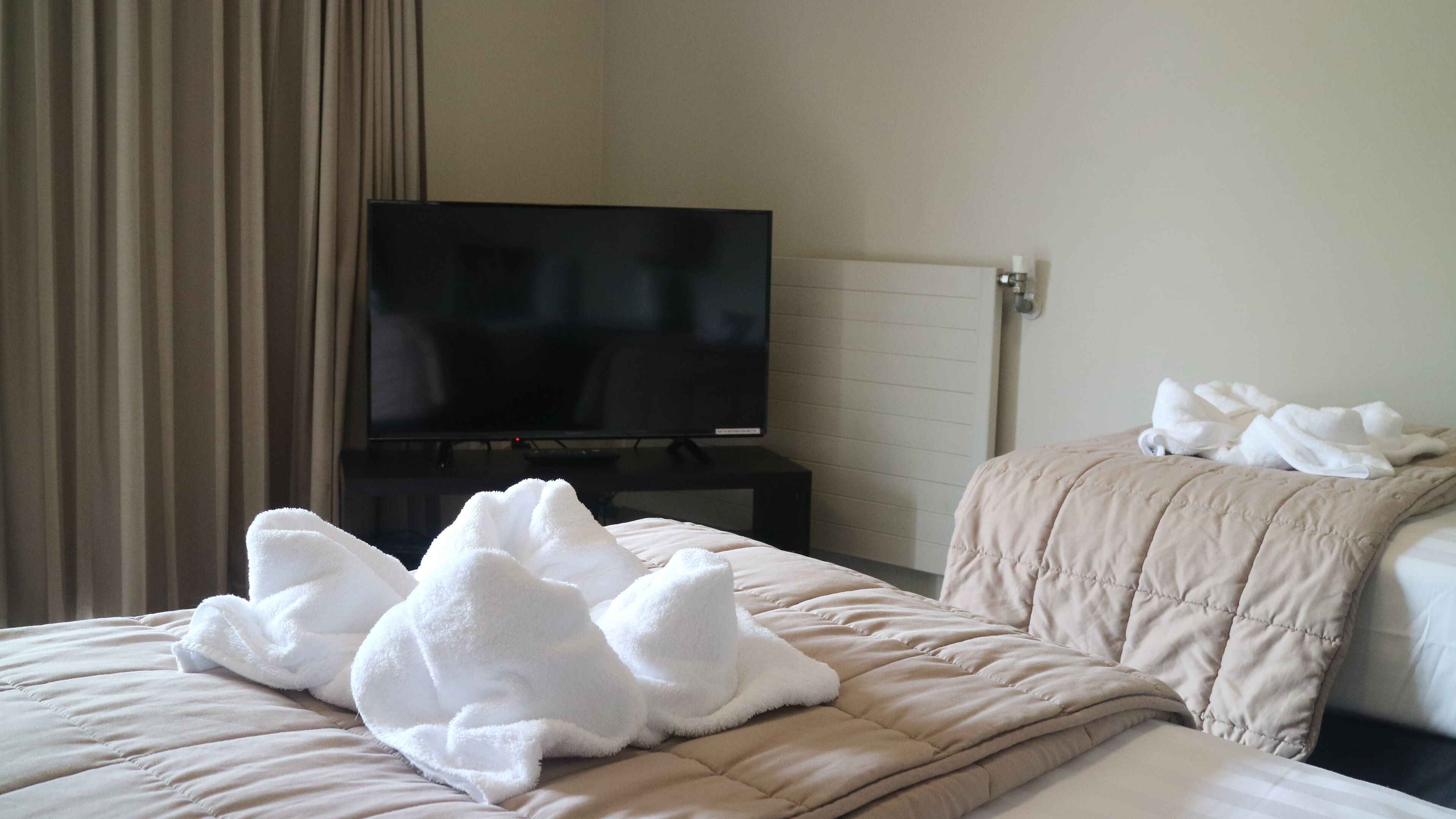 Habitació d'hotel amb un llit, una televisió sobre un suport i una finestra amb cortines.