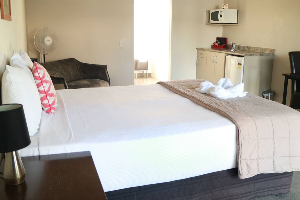 A hotel room with a bed, a desk, a chair, a microwave, and a fan.