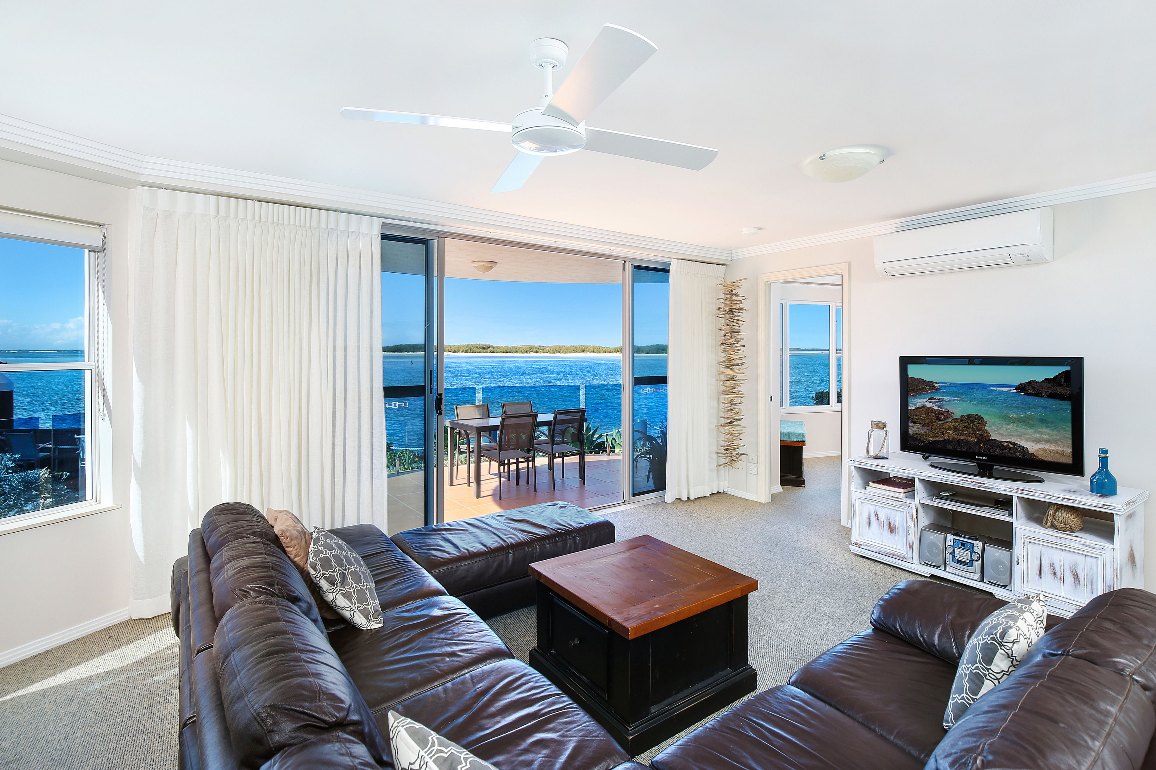 A living room with a large window, a ceiling fan, a flat-screen TV, and a wooden coffee table.