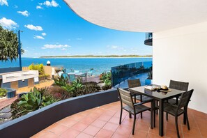 A terrace with a table and chairs overlooking a beach and the sea. - Watermark Resort Caloundra (Caloundra)