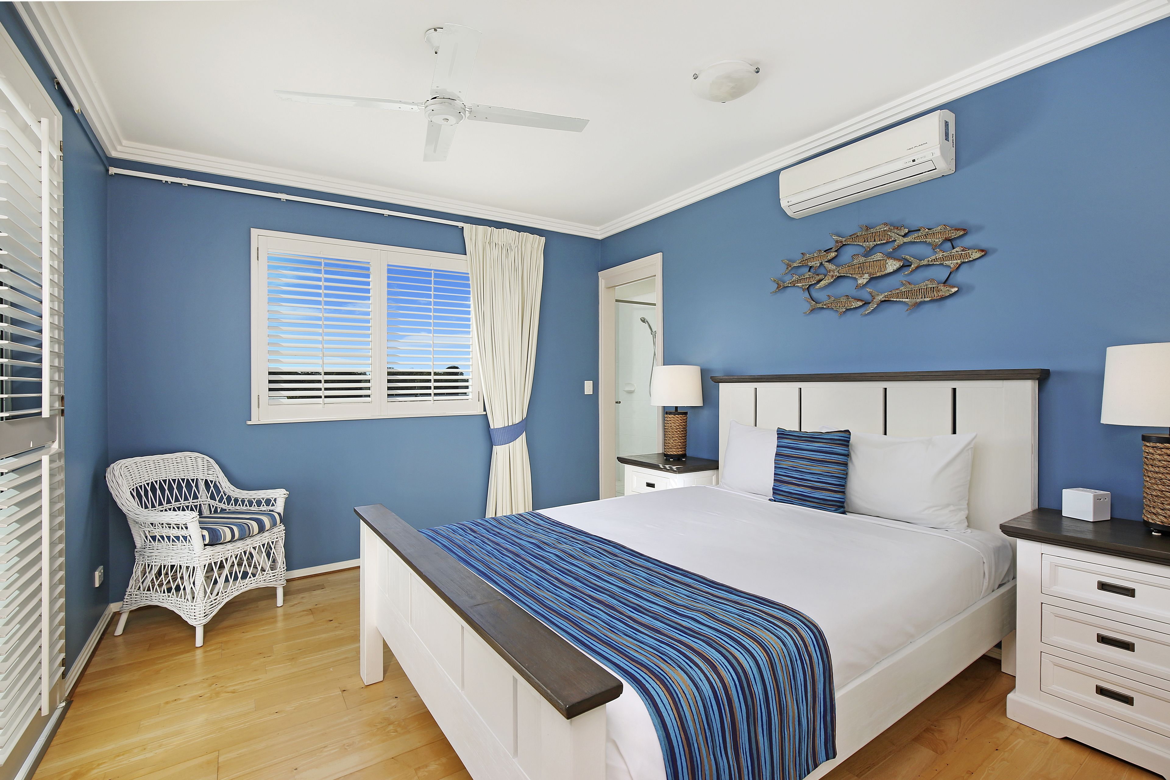 A bedroom with a large bed, a white chair, a ceiling fan, and a window with blinds.