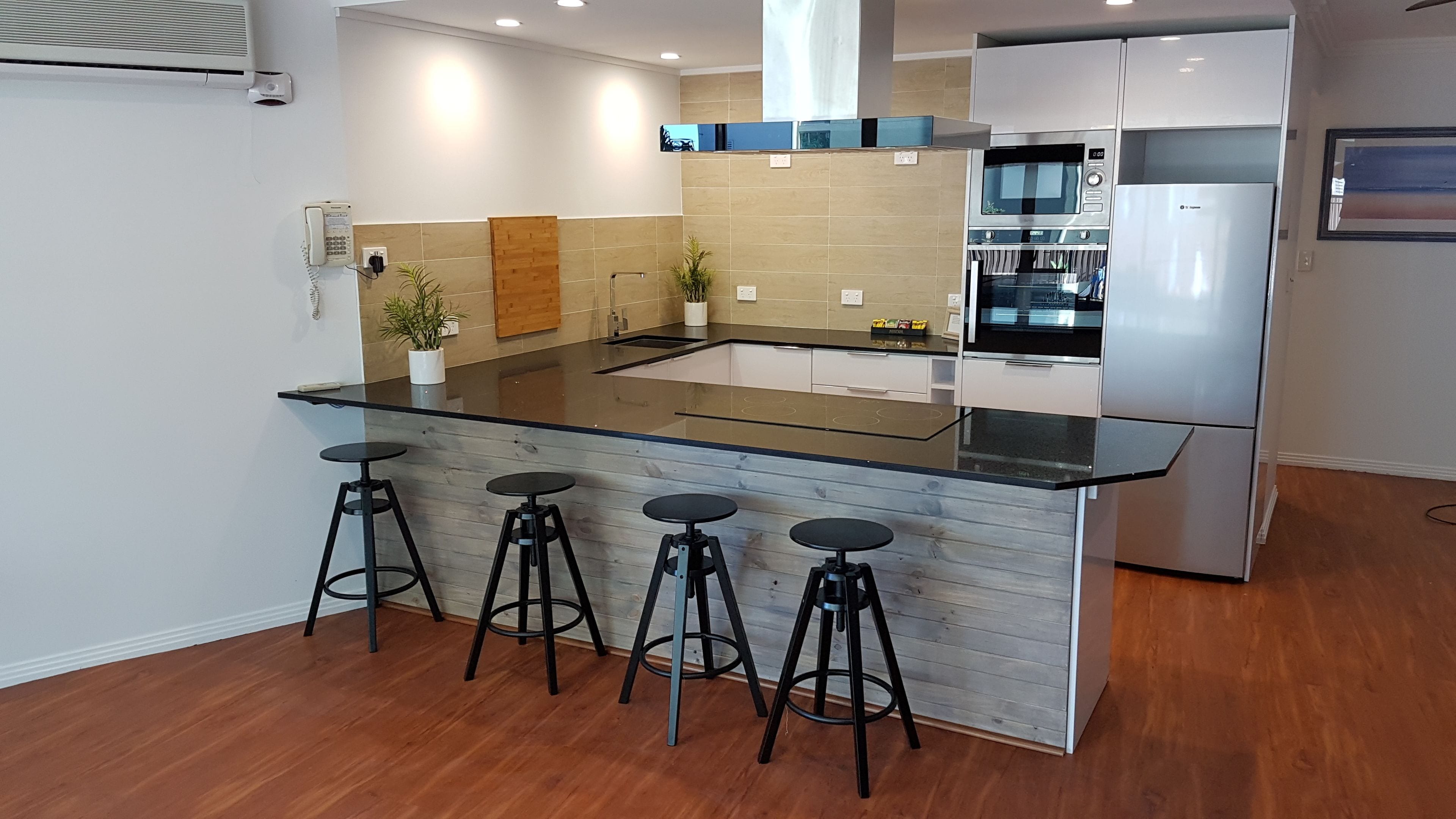 A modern kitchen with a central island, bar stools, stainless steel appliances, and wooden accents.