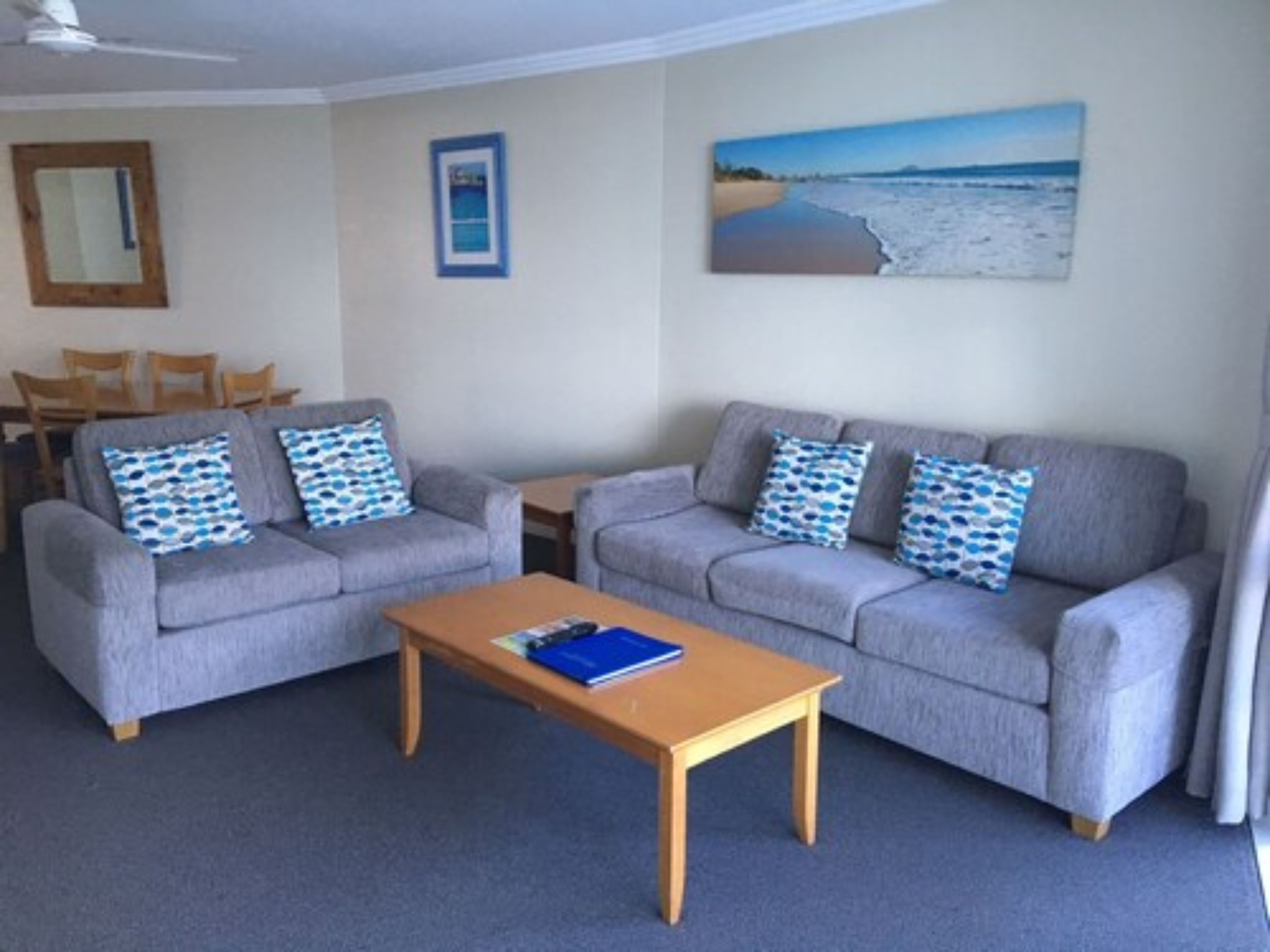 A living room with two grey sofas, a wooden coffee table, and a painting of a beach scene on the wall.