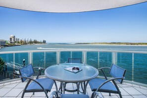 A glass-enclosed balcony with a round table and four chairs, overlooking a coastal area with buildings and a beach. - Watermark Resort Caloundra (Caloundra)