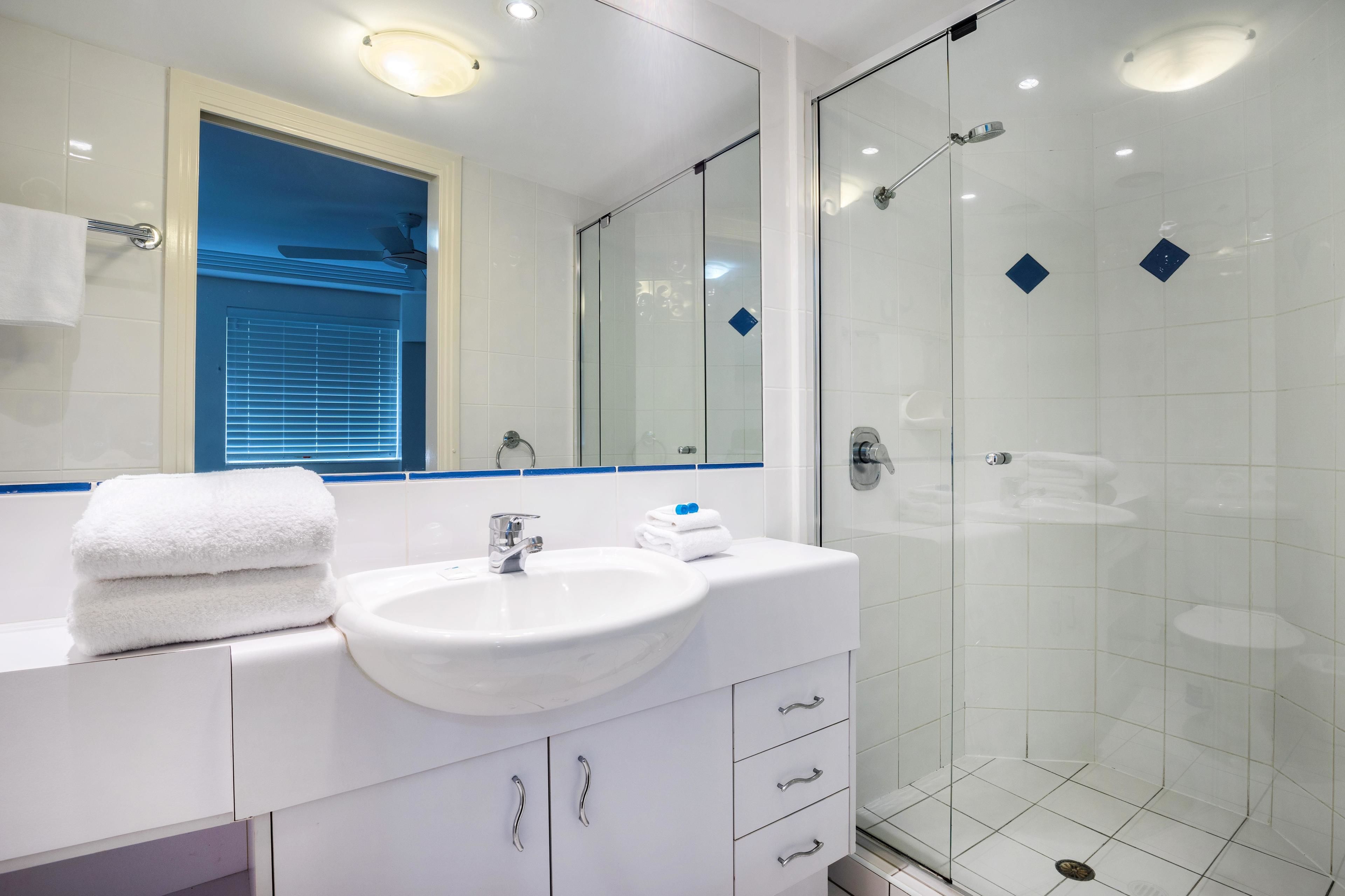 A modern bathroom with a white sink, a glass shower enclosure, and a mirror above the sink.