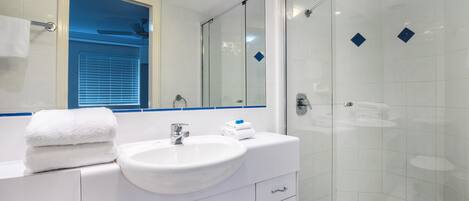 A modern bathroom with a white sink, a glass shower enclosure, and a mirror above the sink.