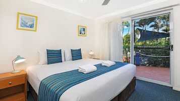 A hotel room with a large bed, a nightstand, a desk lamp, and a view of the outdoor area through a sliding glass door.