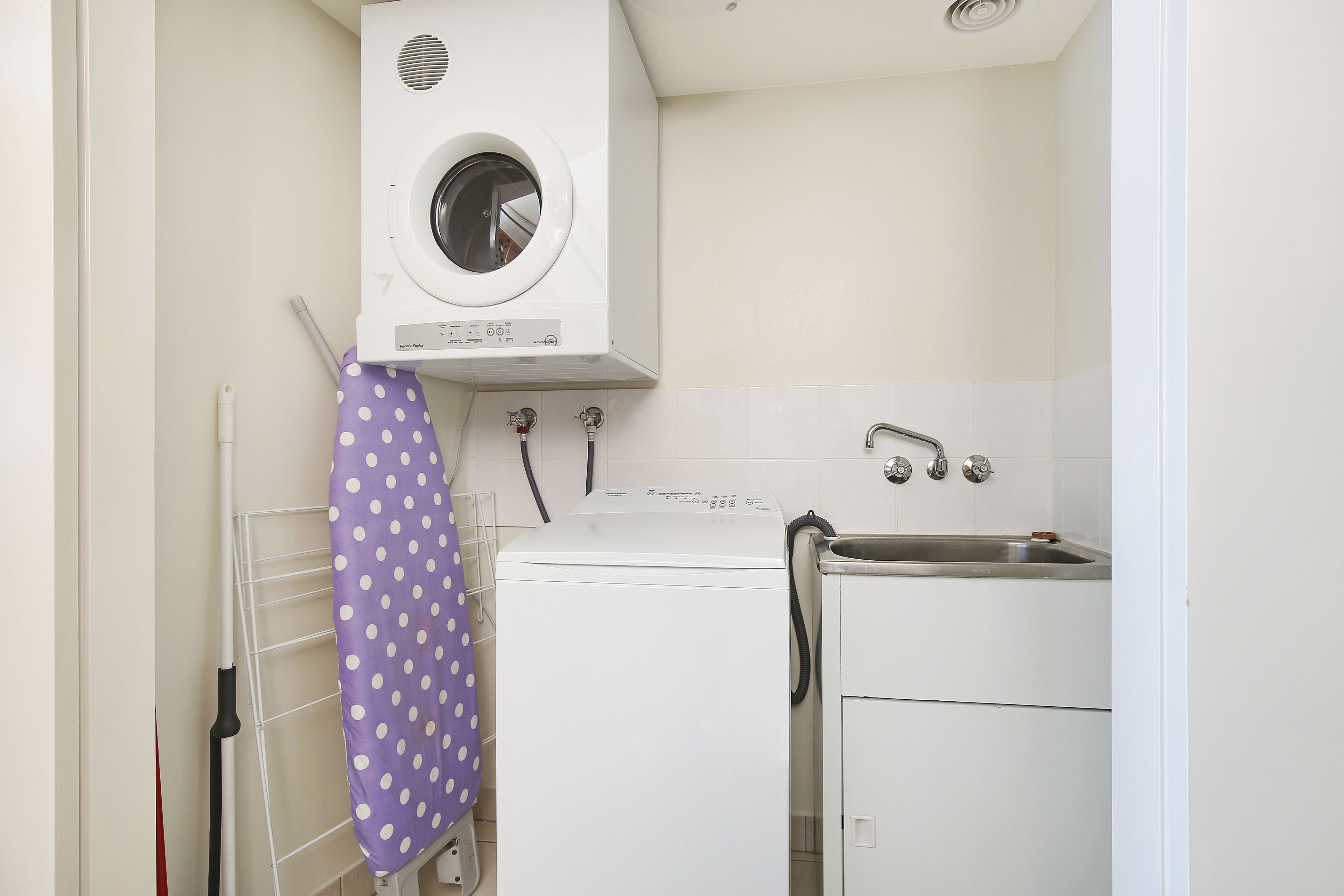 Un espace buanderie compact comprenant un lave-linge, un étendoir et un évier.