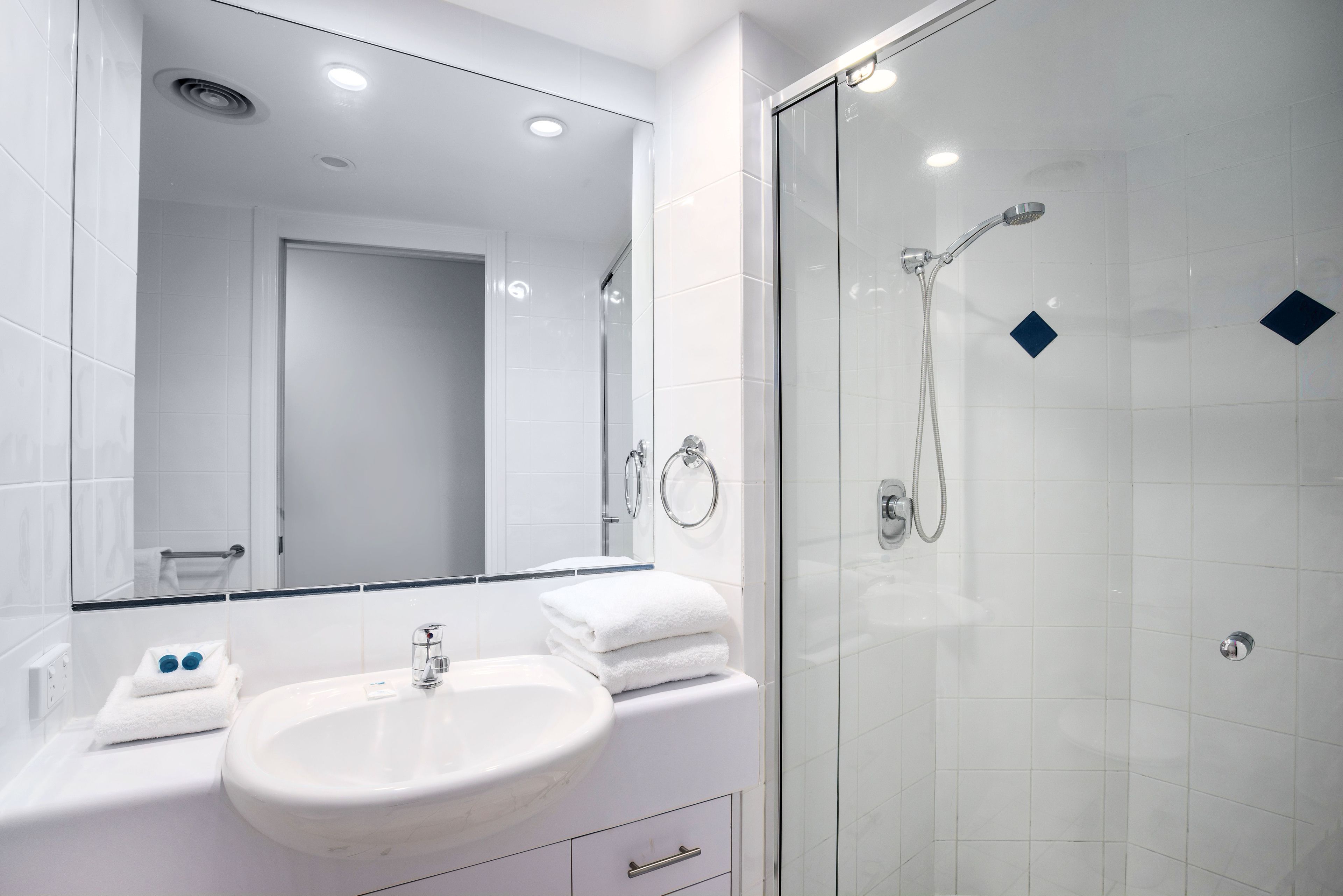 A modern bathroom with a white sink, mirror, and glass shower enclosure.