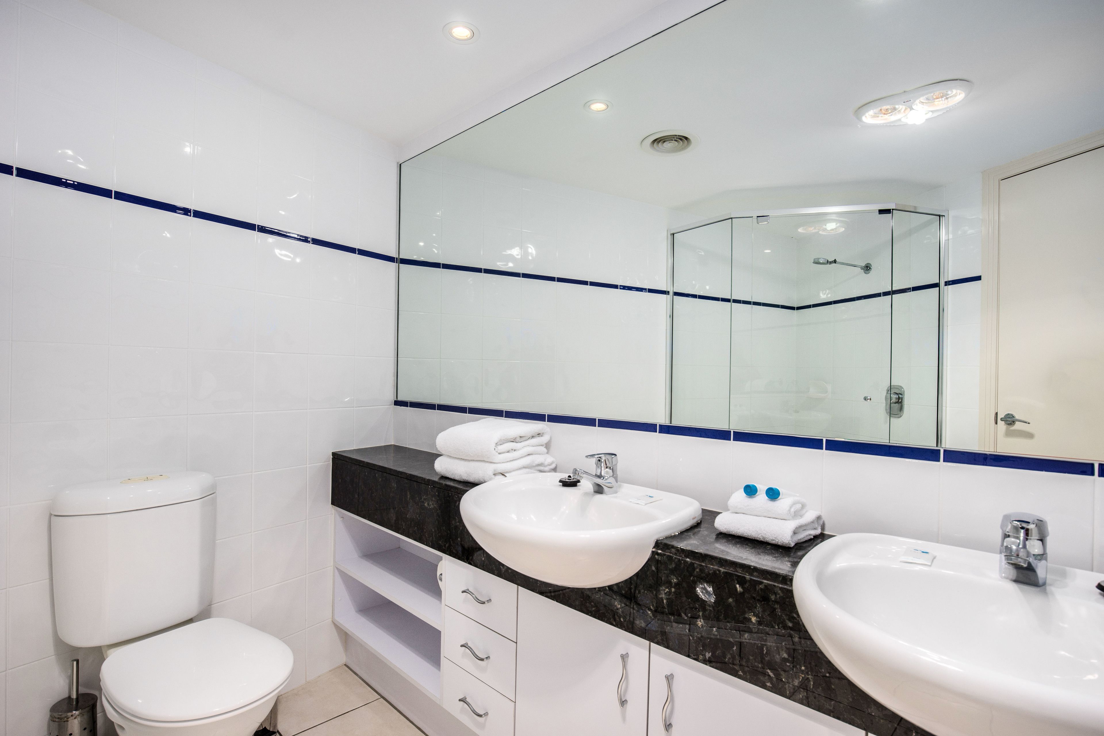 Une salle de bain moderne avec deux lavabos, des toilettes et une douche à parois de verre.