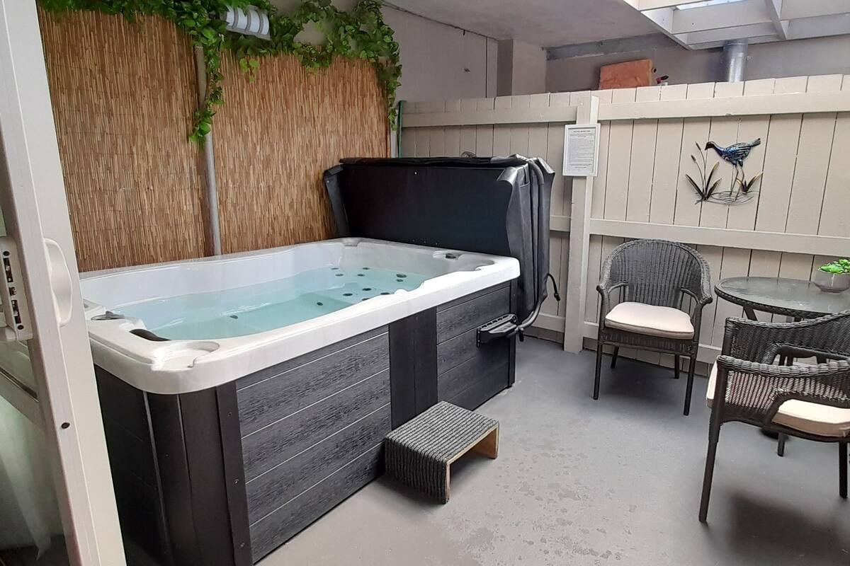 A hot tub area with a wooden wall, a chair, a small table, and a decorative bird sculpture.