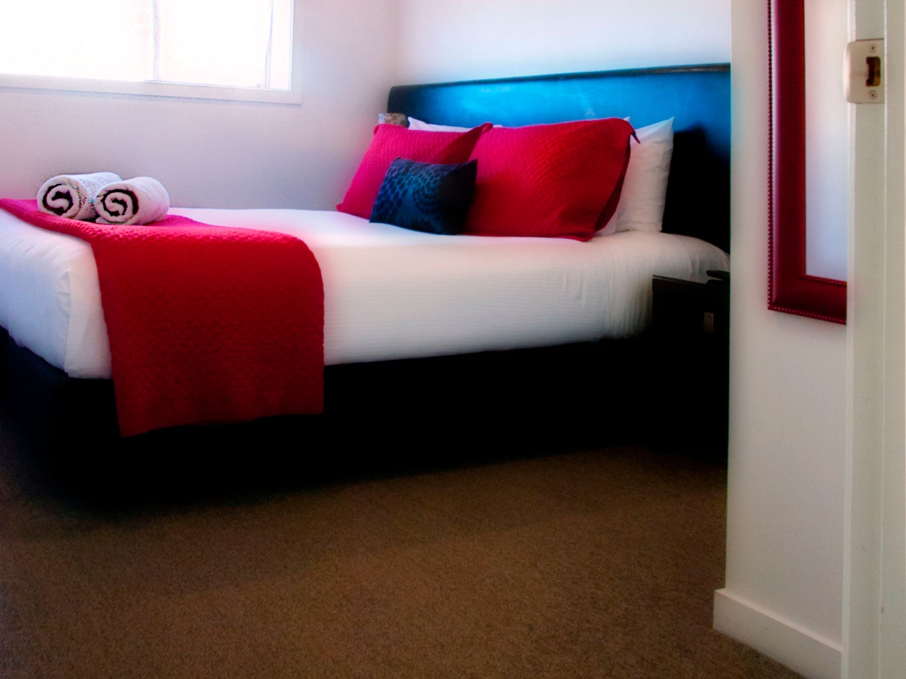 Uma cama com colchão branco, almofadas vermelhas e azuis e um cobertor vermelho.