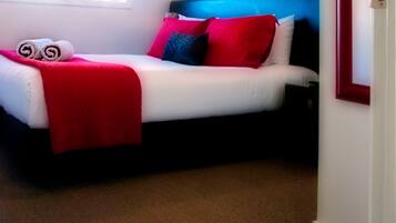 Uma cama com colchão branco, almofadas vermelhas e azuis e um cobertor vermelho.